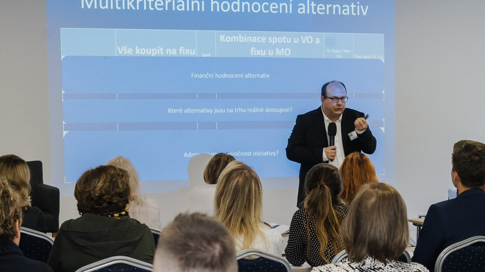 Plný sál na školení Nákupní kliniky, na plátně slide Multikriteriální hodnocení alternativ s tabulkou kritérií.