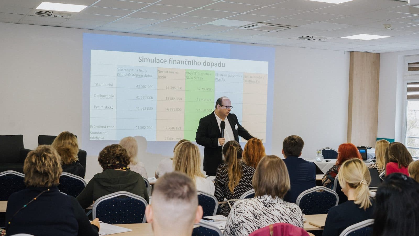 Jan Vašek u plátna s tabulkou Simulace finančního dopadu, plný sál účastníků školení
