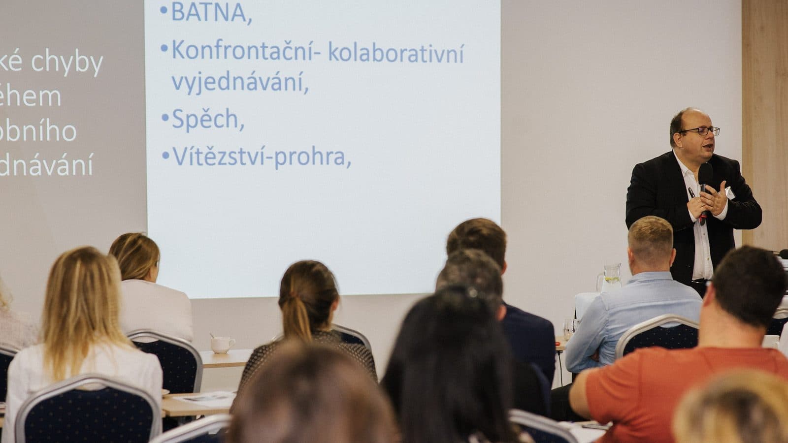 Jan Vašek u plátna na školení vyjednávání, na slidu pojmy BATNA a konfrontační vyjednávání, sál plný účastníků.